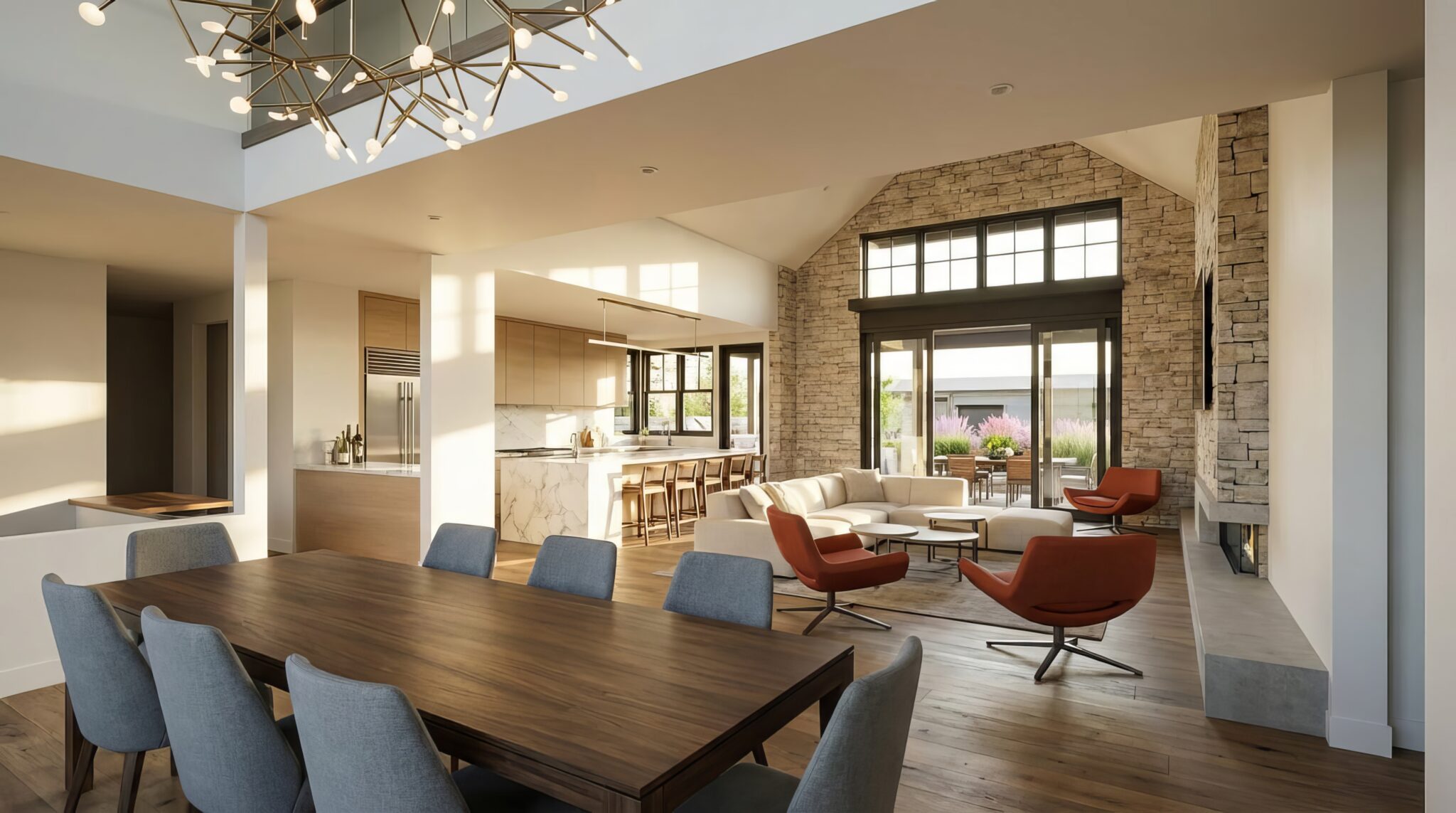 HiveleyInteriorGZe7VYGjpgP7yh0nHsu5w_HoNnRAPA_00001-topaz-upscale-34x 1 - Stillwater Dwellings Open-plan living and dining area with a long wooden table, blue chairs, and a modern chandelier in a bright space with a stone fireplace and large windows.